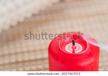 Furious smoking red candle stands on the bamboo tablecloth on the table.