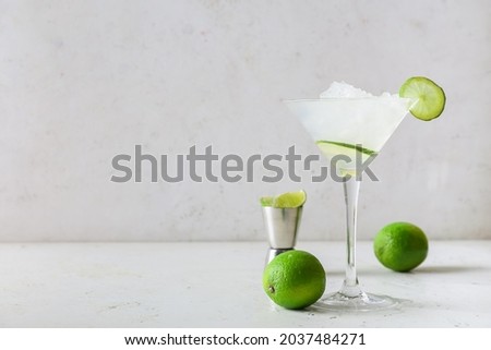 Glass of tasty margarita cocktail and limes on light background