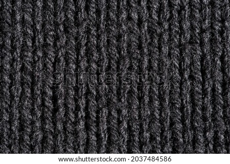 Knitted fabric made of black wool threads, background structure, close-up macro view