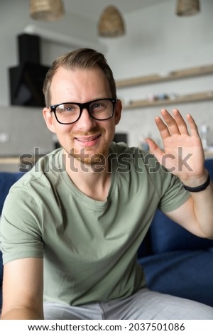 A cheerful guy is waving hello into webcam, smiles and greeting. Video call, video conference, online meeting. Vertical photo, phone screen Royalty-Free Stock Photo #2037501086