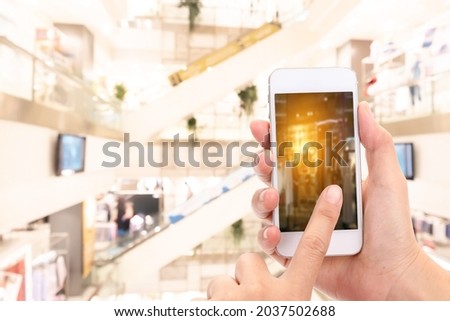 Woman hands Taking a picture with a smart phone in shopping mall with blurred image of clothes shop.