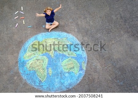 Little preschool girl with earth globe painting with colorful chalks on ground. Positive toddler child. Happy earth day concept. Creation of children for saving world, environment and ecology.