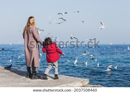 Mother and son walk to the seaside. Birds flying above the water. Cold season vacations Royalty-Free Stock Photo #2037508460