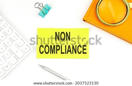 Sticker with the text NON COMPLIANCE on white background, near calculator and notebook