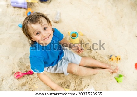 Portrait of preschool toddler boy sitting in a sandbox and playing alone with pleasure. Outdoor educational games for children.