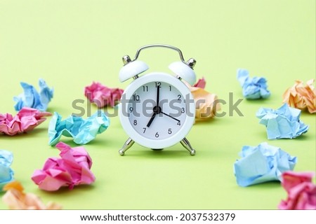 Vintage white alarm clock on a background of crumpled multicolored stickers. Office background or the concept of study and school.