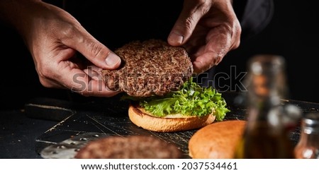 Chef making a burger with a succulent homemade grilled beef patty placing it on top of fresh lettuce on a toasted bun in close up on his hands
