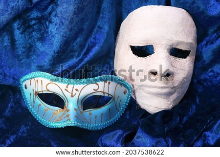 ORNATE TURQUOISE MASK CONTRASTED WITH A STARK WHITE PLASTER OF PARIS MASK ON CLOTH BACKGROUND