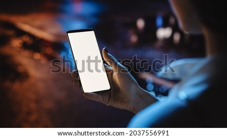 Beautiful Woman using Chroma Key Smartphone while Walking Through Night City Street Full of Neon Light. Female Using White Screen Mobile Phone. Over the Shoulder Close-up Shot