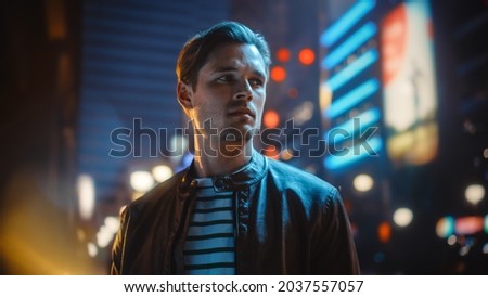 Portrait of Handsome Serious Man Standing, Looking Around Night City with Bokeh Neon Street Lights in Background. Focused Confident Young Man Thinking. Portrait Shot. Royalty-Free Stock Photo #2037557057