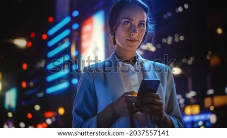 Beautiful Young Woman Using Smartphone Standing on the Night City Street Full of Neon Light. Portrait of Gorgeous Smiling Female Using Mobile Phone.