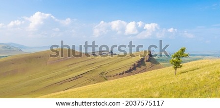 Summer panoramic view of the Sunduki mountain range located in the valley of the Bely Iyus River in Khakassia, Russia. Landscape of green hills under blue sky with white fluffy clouds