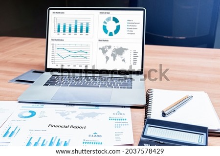 Mock up sales summary slide show presentation on display laptop with calculator and paperwork on table in meeting room