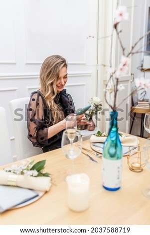 Beautiful stylish woman sitting at table using smartphone during dinner