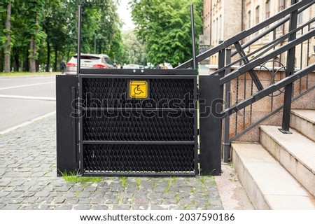 Electric platform lift at building staircase for disabled people with wheelchair sign plate on old city street. Elevator stairlift ramp mechanism for senior disability people. Medical urban equipment