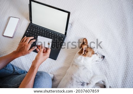 top view of unrecognizable woman doing online shopping with credit card and laptop. Cute small jack russell dog sleeping on bed.Technology and business concept