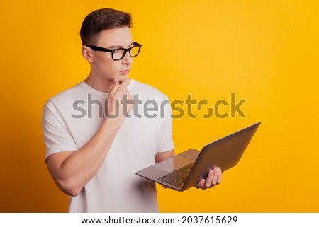 Portrait of minded smart freelancer guy hold netbook finger chin think on yellow background