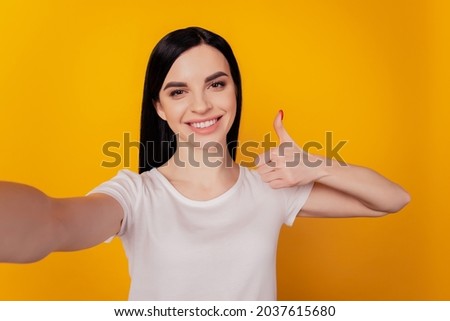 Self portrait of positive toothy girl shooting selfie on front camera smile show thumb-up isolated on yellow background