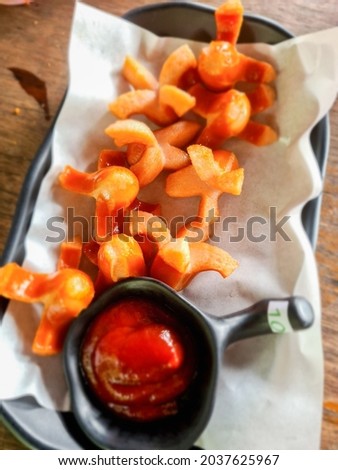 Sausages cut into pieces and ketchup in a plate with greaseproof paper 