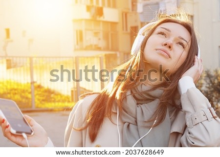 Caucasian Young Girl Listening Track or Podcast With White Over-Ear Headphone In Green Public Garden. Leisure Meditation for Calming Down and Relaxing. Mindfulness and Music Therapy.