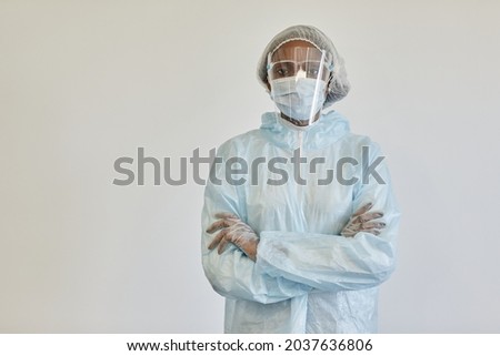 Serious nurse in PPE suit, medical mask and gloves, crossing arms and looking at camera, isolated of white