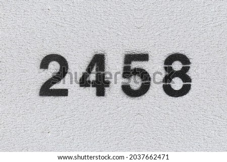 Black Number 2458 on the white wall. Spray paint. Number two thousand four hundred and fifty.