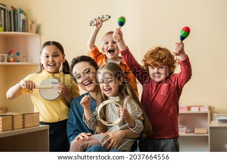 excited multiethnic kids playing musical instruments near happy teacher Royalty-Free Stock Photo #2037664556