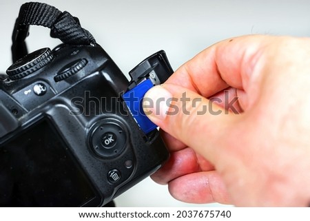 Photographer inserting or removing a blue memory card into the slot in the camera. Data storage and protection. Photographic equipment and technology