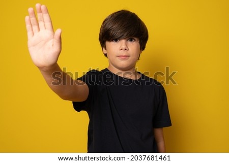 Child looking at camera. Stop signal with his hand over yellow background