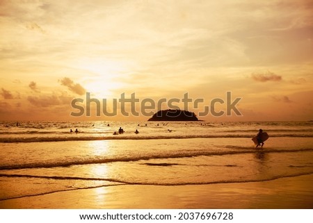 Surfboard on tropical beach in summer beach sunset.Landscape sunset or sunrise light of nature cloudscape sky.Burning sky and shining golden waves.Sun over mountain silhouette paradise island.