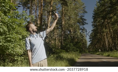 Serious man holding phone up to find mobile network in forest, tourist got lost