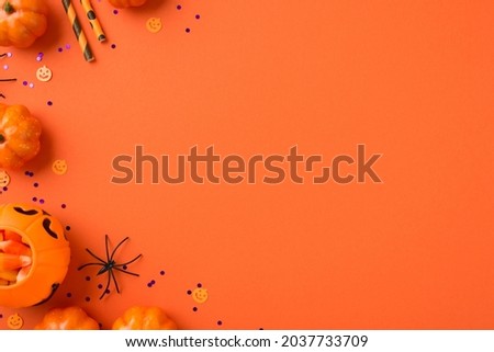 Top view photo of halloween decorations pumpkin basket with candy corn straws spider and violet sequins on isolated orange background with empty space