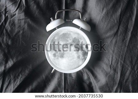 A glowing moon inside the alarm clock on the bed. Sleep time. Night rest. Waking up at night, insomnia. A nightmare. Creative alarm clock. Royalty-Free Stock Photo #2037735530
