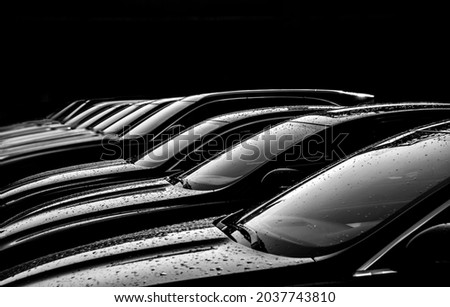 Black sedan cars standing in a row. Fleet of generic modern cars. Transportation. Luxury car fleet consisting of generic brandless design. isolated in dark background. after rain. wet surface. Royalty-Free Stock Photo #2037743810