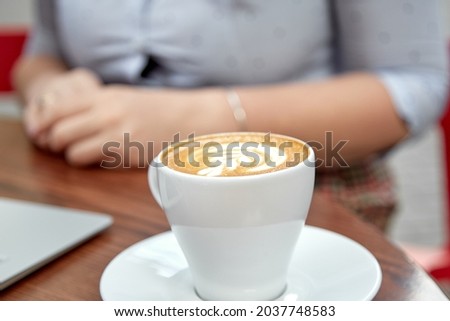 White mock up of cup of coffee on the table outside in foreground of women background. Copy space. Autumn coziness. Place for advertising. High quality photo