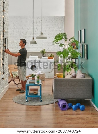 Man is hanging frame in the decorative room, sofa and washing machine background.
