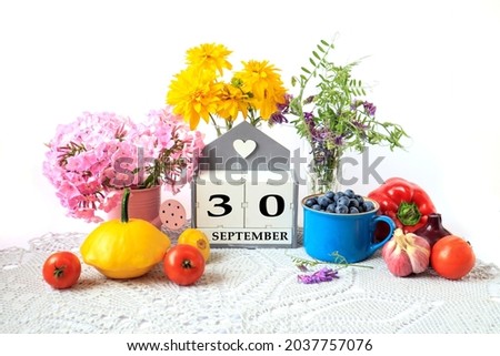 Calendar for September 30 : the name of the month in English, cubes with the number 30, ripe vegetables, bouquets of various flowers, blueberries in a blue cup on a gray napkin, white background
