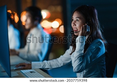 Millennial Asia young call center team or customer support service executive using computer and microphone headset working technical support in late night office. Telemarketing or sales job concept. Royalty-Free Stock Photo #2037759398