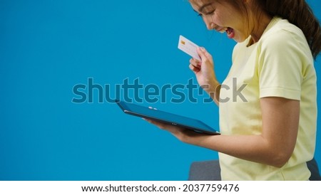 Young Asia lady using tablet and credit bank card with positive expression, smile broadly, dressed in casual clothing and stand isolated on blue background. Happy adorable glad woman rejoices success.