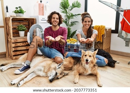 Young hispanic couple doing laundry with dogs smiling with hands palms together receiving or giving gesture. hold and protection 