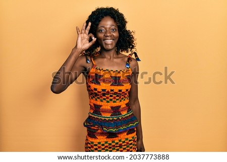 Young african american woman wearing traditional african clothes smiling positive doing ok sign with hand and fingers. successful expression. 