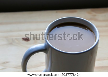 White cup of coffee with milk closeup on a wooden surface with natural window light