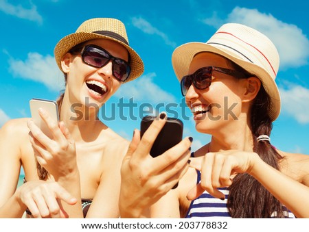 Summer, holidays, vacation and happiness concept - Pretty girls using smart phone mobile at the beach.