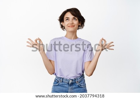 Young happy, calm woman meditating, looking up with relaxed face, holding hands sideways in zen, nirvana lotus pose, practice yoga, standing over white background.