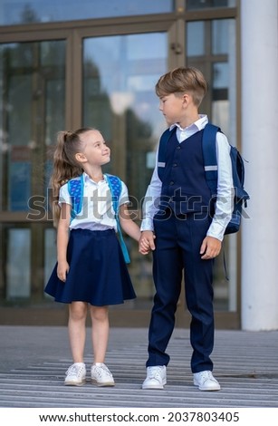 Elder brother and little sister stand in front of the school building holding hands Royalty-Free Stock Photo #2037803405