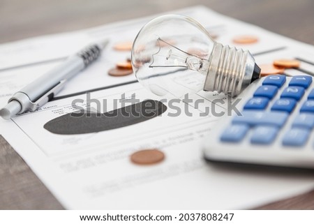 A light bulb, a pen, a calculator and some copper euro cent coins lie on top of an electricity bill. Royalty-Free Stock Photo #2037808247