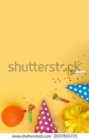 Colorful happy birthday or party background Flat Lay with birthday hats, blowers, confetti and ribbons on yellow background. Top View with Copy space.
