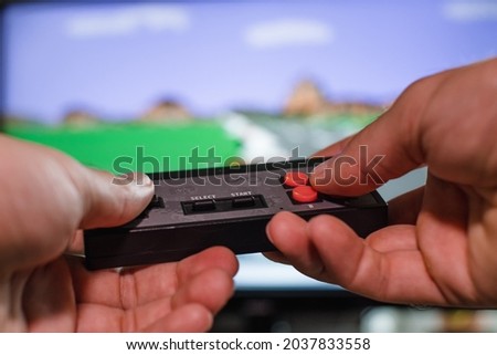 A man's hands hold a game console controller against the background of a TV screen with a video game. Home entertainment concept