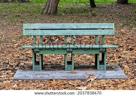 A horizontal shot of a rusty old blue wooden seat on old yellow fallen leabes in the park