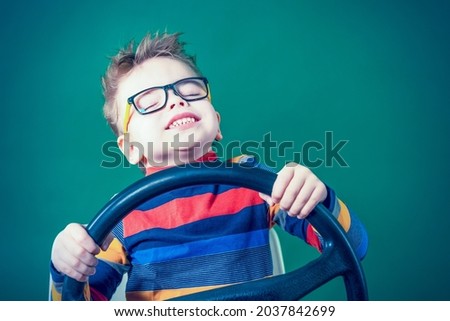 Happy boy wearing glasses enjoys the game pretending to be a car driver close-up on a green background